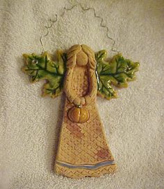 a ceramic angel ornament hanging on a white towel with green leaves and acorns