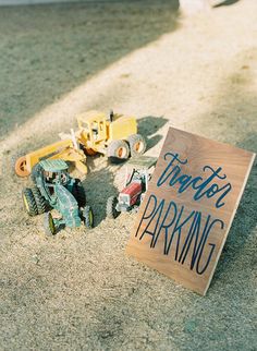 a wooden sign that says trash and parking next to toy trucks on the ground with a construction truck in the background