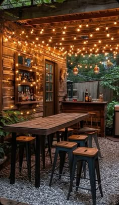 an outdoor dining area with lights strung from the ceiling and wooden table surrounded by stools