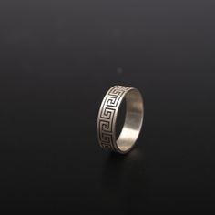 a silver ring with an intricate design on the outside and inside, sitting on a black surface