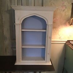 an old white china cabinet with glass doors and shelves on the top, next to a lamp