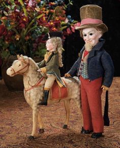 two figurines are sitting on top of a horse and one is wearing a top hat