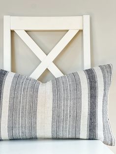 a white chair with a black and white striped pillow on top of it next to a wooden headboard