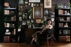 a woman sitting at a desk in front of a book shelf filled with books and pictures