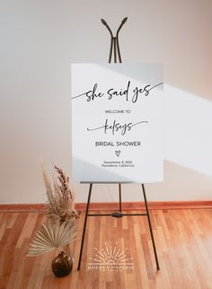 a white sign sitting on top of a wooden floor next to a vase filled with flowers