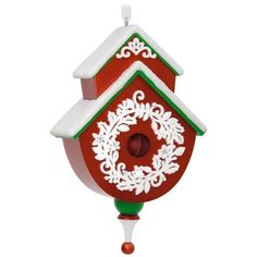 a red and green birdhouse with snow on the roof is hanging from a chain