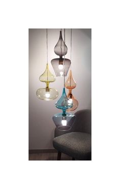 three different colored glass lamps hanging from a ceiling fixture in a room with a gray chair