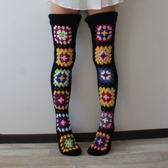 a woman's legs with colorful crocheted socks and stockings on, standing in front of a white wall