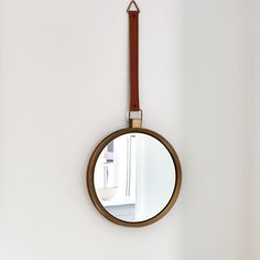 a round mirror hanging on the wall with a leather strap around it's neck