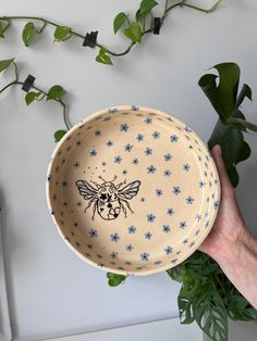 a hand holding a bowl with a bee design on the front and blue flowers on the outside