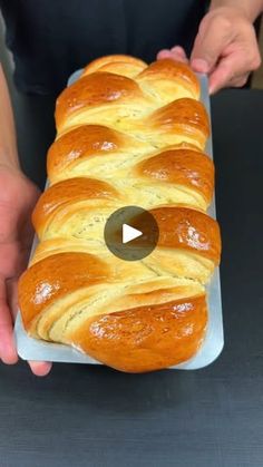 a person holding a loaf of bread on top of a pan filled with buttered pretzels