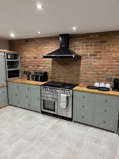 a kitchen with grey cabinets and a stove top oven next to a brick walled wall