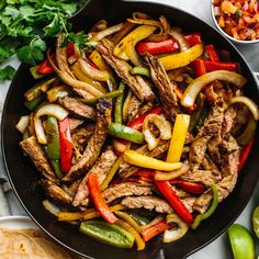 steak fajita in a skillet with peppers, onions and cilantro