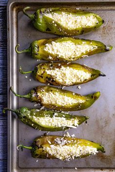 four green peppers covered in cheese and parmesan on a baking sheet, ready to go into the oven