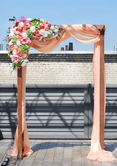 an outdoor wedding ceremony setup with pink and white flowers on the top of a wooden structure