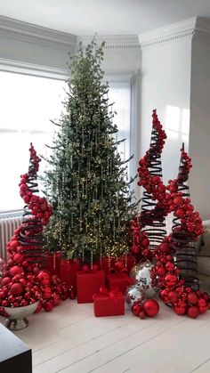 a christmas tree surrounded by red and silver ornaments in front of a white wall with windows