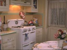 a white stove top oven sitting inside of a kitchen next to a table with flowers on it