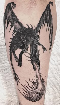 a black and white photo of a dragon tattoo on the leg with flames coming out of it