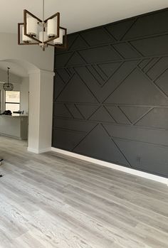 an empty room with hard wood floors and black wallpaper on the walls, in front of a chandelier