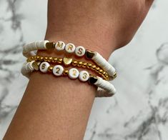 two white and gold beaded bracelets with the word msm on them, sitting next to each other