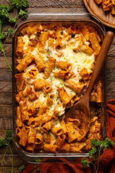 a casserole dish filled with pasta and cheese on a wooden table next to two serving spoons