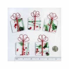 four wrapped gift boxes with red ribbon and holly on them next to a quarter penny