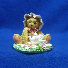 a teddy bear with a tea cup and saucer sitting on a blue cloth background