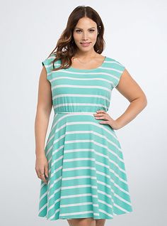 a woman in a green and white striped dress with her hands on her hips, posing for the camera