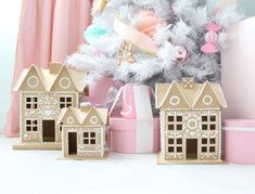 three gingerbread houses are next to a christmas tree with ornaments on it and pink presents