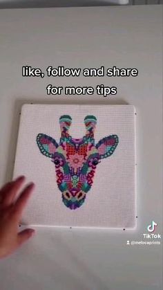 a hand is holding up a cross - stitch giraffe on a white surface