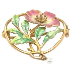 This enchanting brooch is a quintessential example of Art Nouveau jewellery, crafted from 15-carat yellow gold. The piece is a celebration of nature, art, and craftsmanship, capturing the fluid and organic lines characteristic of the Art Nouveau movement. At the heart of the brooch lies an intricate floral and leaf design, beautifully detailed to reflect the natural world. The gold forms delicate, sinuous lines that intertwine and flow, creating a harmonious and elegant composition. Adding to the brooch's allure is the use of vibrant enamel work. The enamel, applied with meticulous care, brings the flowers and leaves to life with rich, lustrous colours. The enamel's sheen contrasts beautifully with the warm glow of the yellow gold, enhancing the overall visual impact of the piece. Nestled Yellow Gold Enamel Brooches, Art Nouveau Yellow Gold Collectible Brooches, Yellow Gold Flower Brooch Jewelry, Yellow Gold Flower Brooch, Art Nouveau Enamel Brooch Jewelry, Elegant Yellow Gold Enamel Brooches, Unique Yellow Gold Enamel Brooch, Elegant Flower Enamel Pin Collectible, Art Nouveau Yellow Gold Brooches Gift