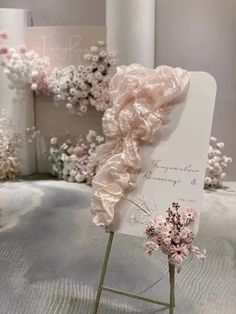 a white sign with pink flowers on it sitting in front of a floral display case