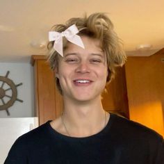 a young man with blonde hair and a white bow on his head smiles at the camera