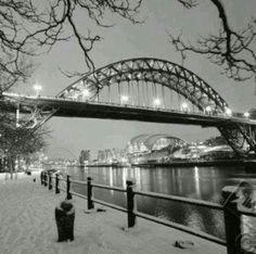 people are walking on the snow covered sidewalk by the water under a bridge at night