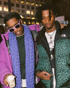 two young men standing next to each other in front of a building wearing sunglasses and scarfs