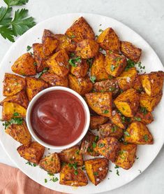 a white plate topped with potatoes covered in ketchup and garnished with parsley