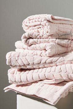 a stack of folded pink towels sitting on top of a white table next to a gray wall