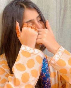 a woman with her hands on her face while wearing an orange and blue patterned shirt