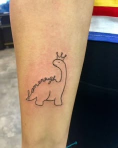 a small dinosaur tattoo on the left inner arm, with words written in cursive font