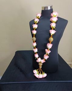 a mannequin with pink flowers on it and a gold beaded necklace hanging from the neck