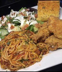 a white plate topped with pasta, chicken and veggies next to a salad