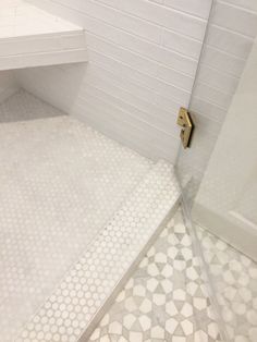 a white tiled bathroom with a shower and toilet in the corner, next to a window