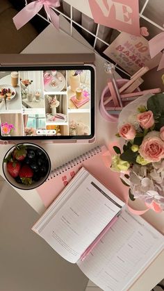 a table topped with flowers and notebooks next to a tablet computer on top of a desk