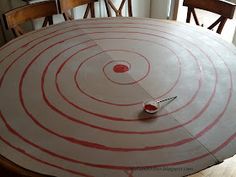 a round table with red lines on it and a knife stuck in the center, surrounded by wooden chairs