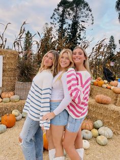 three girls standing in front of hay bales and pumpkins