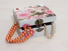 a box with some beads on it and a flowered necklace hanging from the lid