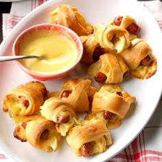 a white plate topped with pigs in a blanket next to a bowl of dipping sauce