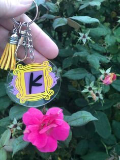 a hand holding a keychain with the letter k on it and a flower