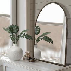 two vases with plants sit on a mantle in front of a large arched mirror