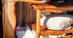 a cat sitting on top of a wooden chair next to a pile of pillows and blankets